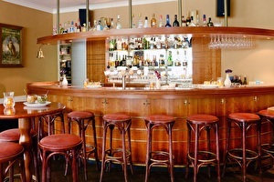 Hotelbar des Amrâth Hotel Lapershoek Arenapark im Restaurant Vivaldi, eine runde Holzbartheke mit Barhockern, an der Rückwand befinden sich Flaschen Wein und Spirituosen.