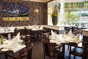 Amrâth Hotel Lapershoek Arenapark Restaurant Vivaldi, Holzstühle und die Holztische sind mit weißen Tischdecken und Servietten gedeckt.