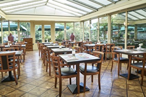 Amrâth Hotel Lapershoek Arenapark Wintergarten im Restaurant Vivaldi, Holztische gedeckt für das Frühstück mit Holzstühlen und einem schwarzen weichen Sitzpolster.