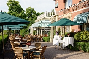 Amrâth Hotel Lapershoek Arenapark Terrasse angrenzend an den Eingang des Hotels und des Restaurants. Grüne Sonnenschirme sind über den Tischen und Stühlen auf der Terrasse ausgeklappt.
