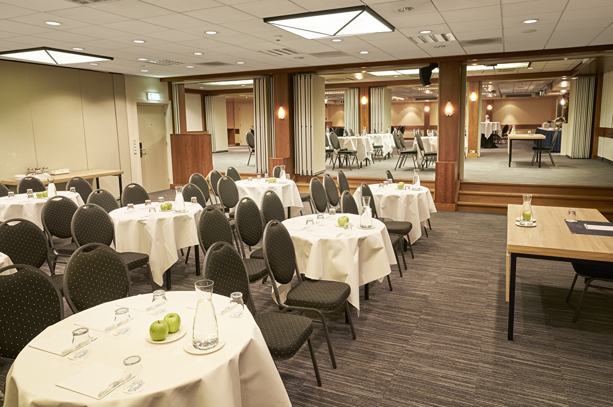 Großer Saal im Amrâth Hotel Lapershoek Arenapark, eingerichtet für Präsentationen oder Workshops mit runden Tischen und Bühnenbereich.