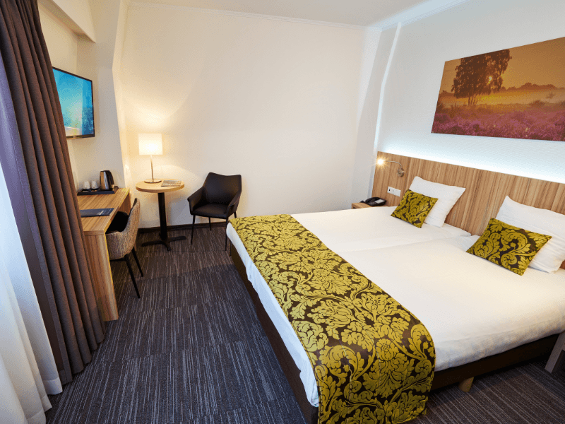 Amrâth Hotel Lapershoek Arenapark Comfort room large double bed with an ornate yellow bedspread and matching small cushions.