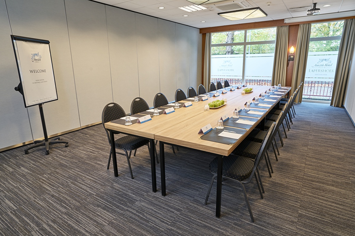 Tagungsraum im Amrâth Hotel Lapershoek Arenapark, mit großer rechteckiger Anordnung, Namensschildern und Blick ins Grüne.