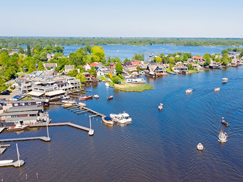 Loosdrechtse Plassen in Hilversum met boten op het water en huizen langs de oever op een zonnige dag.