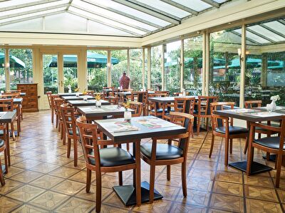 Gezellige serre van Amrâth Hotel Lapershoek Arenapark, met houten tafels en stoelen, veel natuurlijk licht en uitzicht op de groene omgeving.