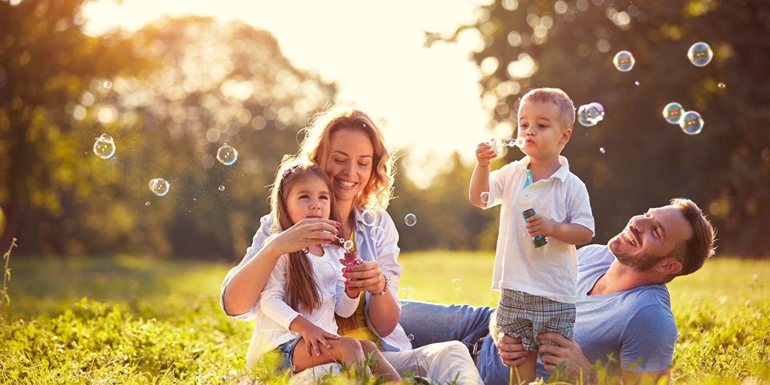 Een familie geniet van een zonnige dag in het gras terwijl ze bellen blazen en samen lachen.