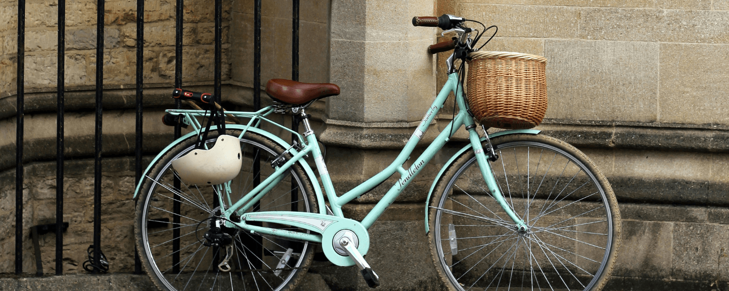 A light green bike parked on the sidewalk leaning against a stone wall.