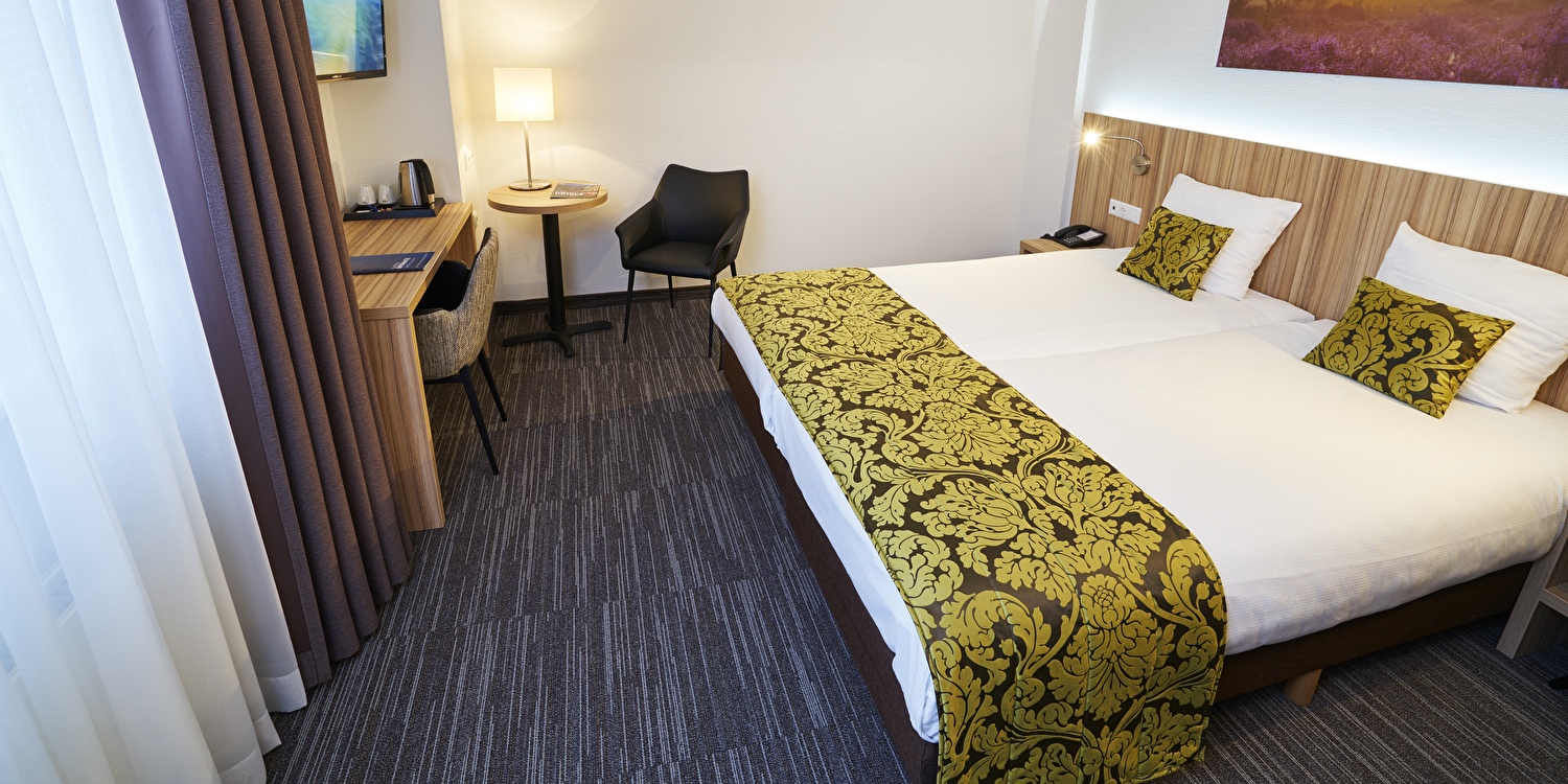 Opgemaakt tweepersoonsbed met een kenmerkende geelgroene sprei en houten hoofdbord in een hotelkamer van Amrâth Hotel Lapershoek