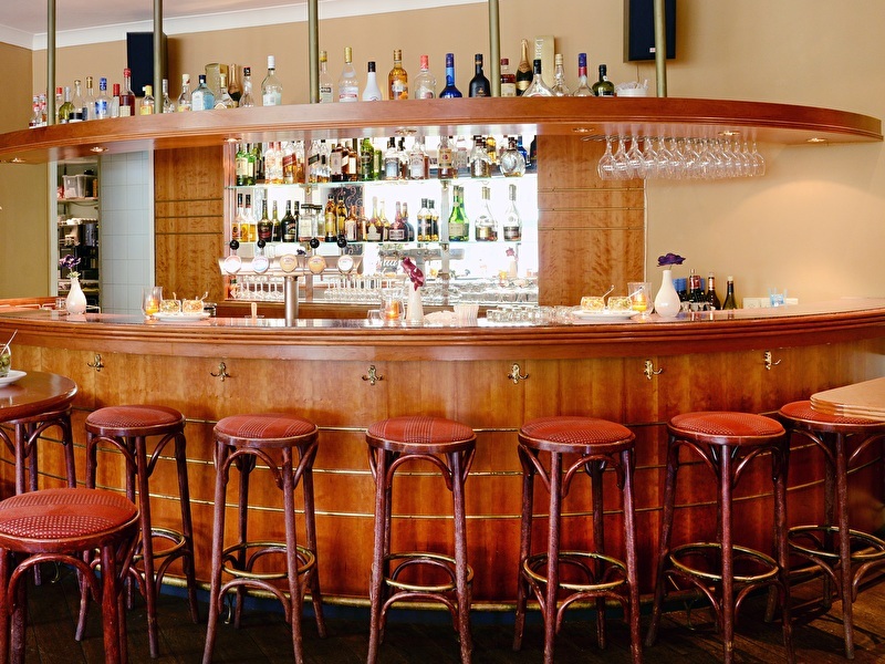 Interieur van de bar bij Amrât Hotel Lapershoek Arenapark: gebogen houten toonbank, rode barkrukken en drankflessen.
