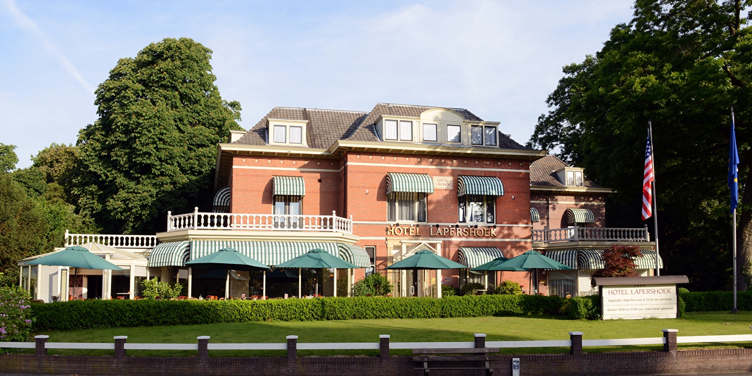 Front facade of Hotel Lapershoek in Hilversum, a classic mansion with green awnings, surrounded by trees
