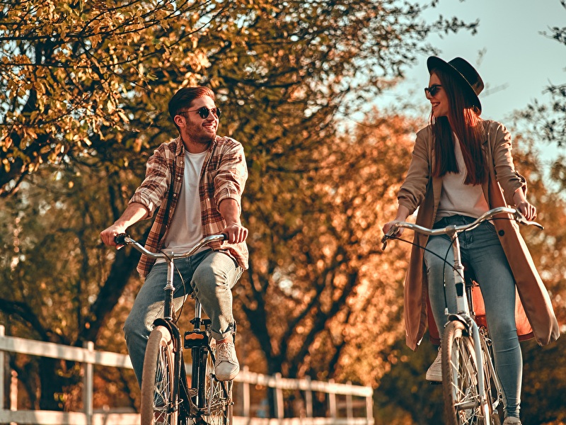Man and woman cycling next to each other laughing on a sunny autumn day.