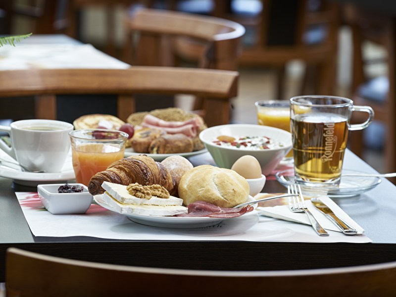 "Gedekte ontbijttafel bij Amrât Hotel Lapershoek Arenapark, met broodjes, beleg, een gekookt ei, muesli en drankjes."