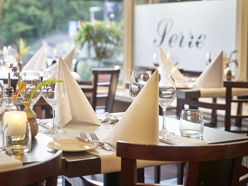 Netjes gedekte restauranttafels bij Amrât Hotel Lapershoek Arenapark, met wit linnen, glazen en bestek.