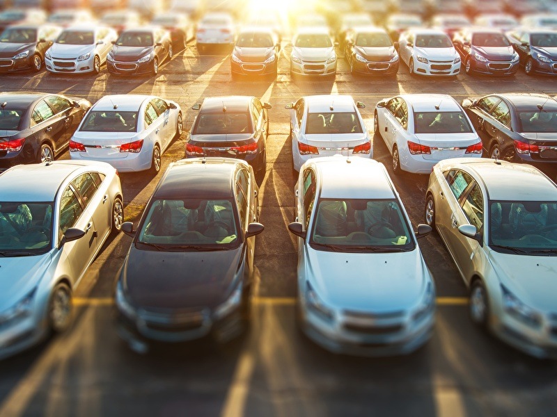 Een parkeerplaats met meerdere rijen met geparkeerde auto's met de ondergaande zon op de achtergrond