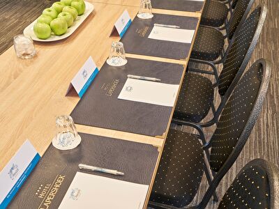 Stijlvolle vergadersetting in Amrâth Hotel Lapershoek Arenapark, met luxe schrijfmappen, naamkaartjes en een schaal verse groene appels op een houten tafel.
